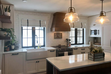 Example of a mid-sized cottage l-shaped vinyl floor and brown floor open concept kitchen design in Other with a farmhouse sink, shaker cabinets, white cabinets, quartzite countertops, white backsplash, ceramic backsplash, paneled appliances, an island and white countertops