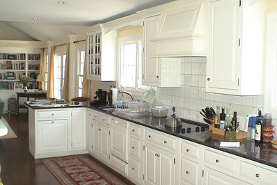 Example of a mid-sized classic l-shaped dark wood floor and brown floor enclosed kitchen design in New York with an undermount sink, raised-panel cabinets, white cabinets, solid surface countertops, white backsplash, subway tile backsplash, white appliances and no island
