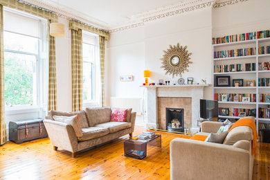 This is an example of a large traditional enclosed living room in Glasgow with white walls, light hardwood floors, a standard fireplace, a stone fireplace surround and a freestanding tv.