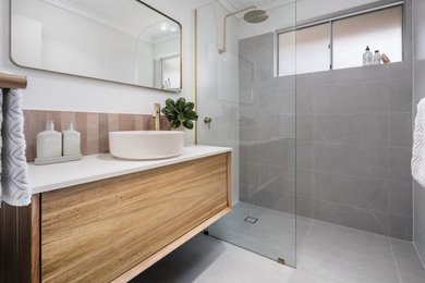 Photo of a mid-sized modern master bathroom in Perth with medium wood cabinets, an open shower, pink tile, ceramic tile, grey walls, ceramic floors, granite benchtops, grey floor, an open shower, white benchtops, a single vanity and a floating vanity.
