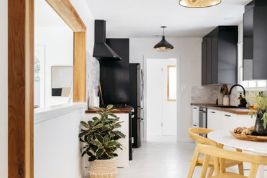 Kitchen - contemporary galley kitchen idea in Los Angeles with black cabinets, wood countertops, gray backsplash and black appliances