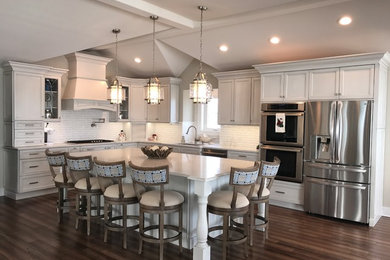 Inspiration for a mid-sized coastal l-shaped medium tone wood floor open concept kitchen remodel in Philadelphia with recessed-panel cabinets, gray cabinets, quartz countertops, white backsplash, stone tile backsplash, stainless steel appliances, an island and an undermount sink