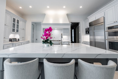 Photo of a large classic kitchen in Dallas with a submerged sink, raised-panel cabinets, grey cabinets, engineered stone countertops, white splashback, glass tiled splashback, stainless steel appliances, porcelain flooring, an island, beige floors and white worktops.