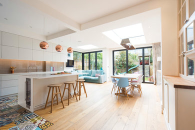 Inspiration for a large eclectic open plan kitchen in London with a built-in sink, light hardwood flooring and an island.