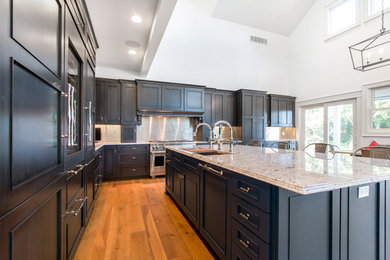 This is an example of a large traditional l-shaped eat-in kitchen in Milwaukee with a single-bowl sink, recessed-panel cabinets, dark wood cabinets, granite benchtops, metallic splashback, metal splashback, panelled appliances, light hardwood floors and with island.