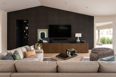 Inspiration for a large transitional open concept light wood floor, brown floor, vaulted ceiling and wallpaper living room remodel in Phoenix with black walls, no fireplace and a wall-mounted tv