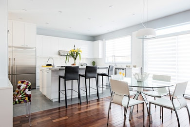 Inspiration for a large contemporary l-shaped medium tone wood floor kitchen remodel in Montreal with flat-panel cabinets, white cabinets, quartz countertops, white backsplash, ceramic backsplash, stainless steel appliances and an island