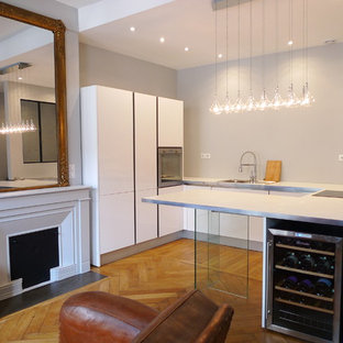 Cette photo montre une cuisine ouverte tendance en U de taille moyenne avec des portes de placard blanches, un évier 1 bac, un plan de travail en stratifié, un électroménager en acier inoxydable, un sol en bois brun et un îlot central.