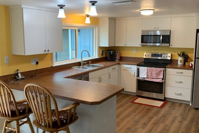 Inspiration for a mid-sized transitional l-shaped laminate floor and brown floor eat-in kitchen remodel in Tampa with a drop-in sink, flat-panel cabinets, white cabinets, laminate countertops, brown backsplash, stainless steel appliances, brown countertops and a peninsula