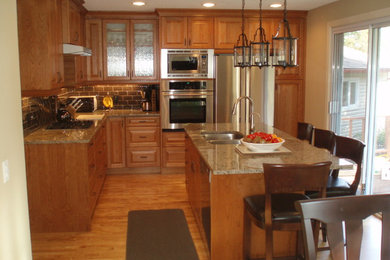 Eat-in kitchen - mid-sized traditional l-shaped medium tone wood floor eat-in kitchen idea in Calgary with an undermount sink, raised-panel cabinets, medium tone wood cabinets, granite countertops, ceramic backsplash, stainless steel appliances and an island