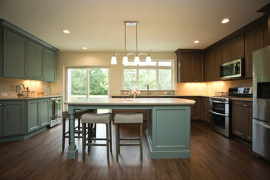 Large transitional u-shaped dark wood floor and brown floor kitchen photo in Portland with an undermount sink, shaker cabinets, medium tone wood cabinets, quartz countertops, brown backsplash, stone tile backsplash, stainless steel appliances and an island
