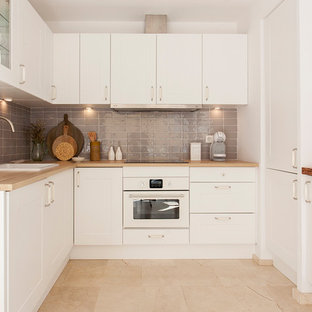 Создайте стильный интерьер: маленькая п-образная кухня в средиземноморском стиле с обеденным столом, монолитной раковиной, плоскими фасадами, белыми фасадами, серым фартуком, фартуком из керамической плитки, белой техникой, полом из травертина, полуостровом и бежевым полом - последний тренд