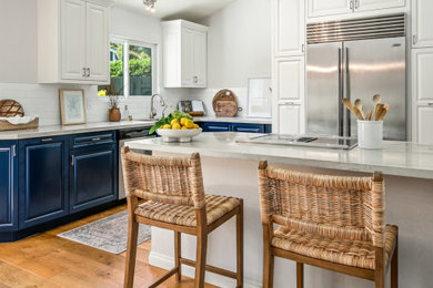 Inspiration for a mid-sized coastal l-shaped medium tone wood floor and brown floor eat-in kitchen remodel in San Diego with a double-bowl sink, raised-panel cabinets, blue cabinets, quartz countertops, white backsplash, subway tile backsplash, stainless steel appliances, a peninsula and white countertops