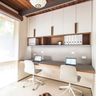Kleines Retro Arbeitszimmer mit weißer Wandfarbe, Teppichboden, Einbau-Schreibtisch, beigem Boden und freigelegten Dachbalken in Melbourne