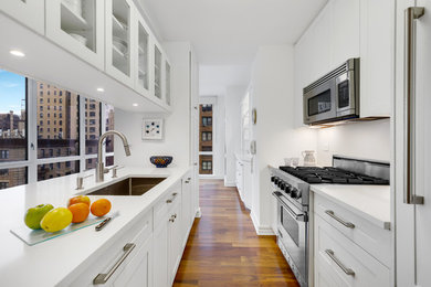 Eat-in kitchen - mid-sized transitional galley medium tone wood floor and brown floor eat-in kitchen idea in New York with an undermount sink, shaker cabinets, white cabinets, quartz countertops, white backsplash, stone slab backsplash, stainless steel appliances, an island and white countertops