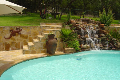 Large tropical backyard custom-shaped lap pool in Dallas with a water feature and natural stone pavers.