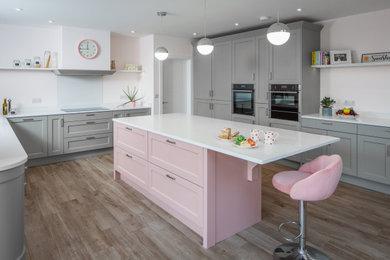 Photo of a large traditional grey and pink u-shaped open plan kitchen in Other with a submerged sink, shaker cabinets, pink cabinets, quartz worktops, white splashback, glass sheet splashback, black appliances, ceramic flooring, an island and white worktops.