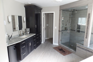 Photo of a large traditional master bathroom in Boston with gray tile, porcelain tile, granite benchtops, recessed-panel cabinets, black cabinets, a drop-in tub, an alcove shower, grey walls, porcelain floors, an undermount sink, grey floor and a hinged shower door.