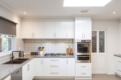 Inspiration for a mid-sized modern u-shaped eat-in kitchen in Melbourne with a double-bowl sink, flat-panel cabinets, white cabinets, quartz benchtops, white splashback, subway tile splashback, no island and grey benchtop.