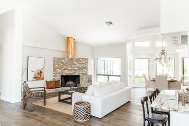 This is an example of a country living room in Phoenix with white walls, medium hardwood floors, a standard fireplace, a brick fireplace surround and brown floor.
