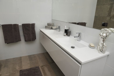 Photo of a mid-sized contemporary 3/4 bathroom in Adelaide with furniture-like cabinets, white cabinets, a corner shower, a one-piece toilet, gray tile, cement tile, white walls, ceramic floors, an integrated sink, solid surface benchtops, grey floor and a hinged shower door.