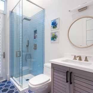 Exemple d'une salle d'eau bord de mer de taille moyenne avec un placard à porte persienne, des portes de placard grises, une douche d'angle, un carrelage bleu, un mur blanc, un lavabo encastré, un WC séparé, un sol en carrelage de porcelaine, un plan de toilette en surface solide et une cabine de douche à porte battante.