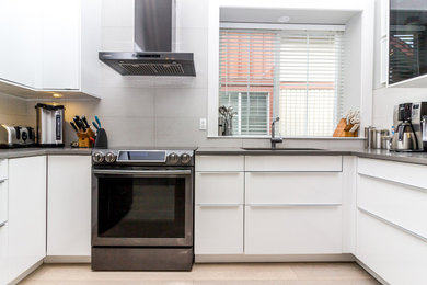 Example of a mid-sized minimalist u-shaped light wood floor, beige floor and vaulted ceiling eat-in kitchen design in Vancouver with an undermount sink, flat-panel cabinets, white cabinets, quartzite countertops, white backsplash, porcelain backsplash, stainless steel appliances, an island and gray countertops
