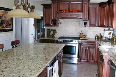Porcelain tile kitchen photo in New York with beige backsplash, stone tile backsplash, an undermount sink, dark wood cabinets, granite countertops, stainless steel appliances and an island