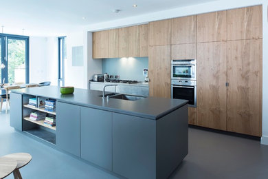 Photo of a contemporary galley eat-in kitchen in Dublin with an undermount sink, flat-panel cabinets, medium wood cabinets, blue splashback, stainless steel appliances and with island.