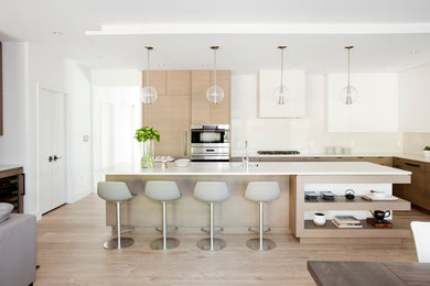 Photo of a mid-sized contemporary l-shaped open plan kitchen in Vancouver with an undermount sink, flat-panel cabinets, light wood cabinets, quartz benchtops, white splashback, glass sheet splashback, stainless steel appliances, light hardwood floors and with island.