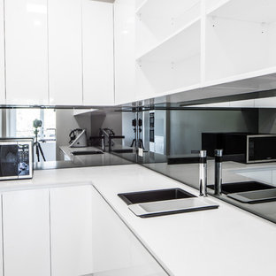 This is an example of a large modern galley kitchen pantry in Sydney with a drop-in sink, flat-panel cabinets, white cabinets, quartz benchtops, black splashback, glass sheet splashback, stainless steel appliances, plywood floors, with island and grey floor.