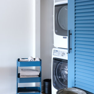 Modelo de armario lavadero tradicional renovado con suelo de madera en tonos medios, lavadora y secadora apiladas, paredes blancas y suelo marrón