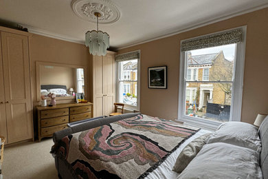Inspiration for a traditional master bedroom in London with pink walls and light hardwood flooring.