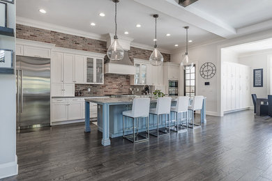 Open concept kitchen - large transitional l-shaped dark wood floor and brown floor open concept kitchen idea in Tampa with a farmhouse sink, shaker cabinets, white cabinets, quartzite countertops, red backsplash, brick backsplash, stainless steel appliances and an island