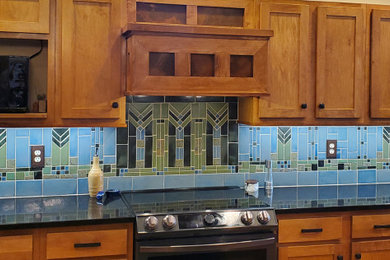 Example of a large arts and crafts l-shaped eat-in kitchen design in Minneapolis with shaker cabinets, brown cabinets, blue backsplash, black appliances, an island, black countertops, a drop-in sink and terra-cotta backsplash