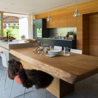 Imagen de cocina comedor actual, grande, con armarios con paneles lisos, puertas de armario negras, encimera de acero inoxidable, salpicadero metalizado, electrodomésticos con paneles, suelo de cemento, una isla y fregadero de un seno