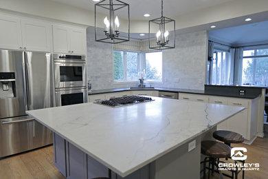 Large transitional l-shaped medium tone wood floor and brown floor eat-in kitchen photo in Portland with an undermount sink, shaker cabinets, white cabinets, quartz countertops, gray backsplash, stainless steel appliances, an island and white countertops