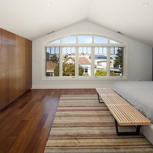 Inredning av ett modernt stort huvudsovrum, med grå väggar, mellanmörkt trägolv, en spiselkrans i sten och en standard öppen spis