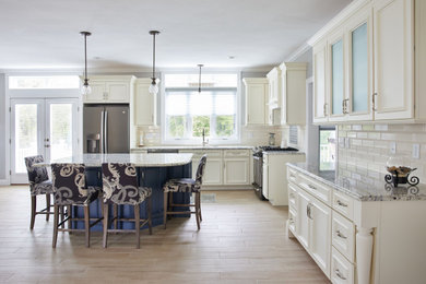 Example of a large classic l-shaped light wood floor eat-in kitchen design in Boston with an undermount sink, recessed-panel cabinets, beige cabinets, granite countertops, beige backsplash, ceramic backsplash, stainless steel appliances, an island and beige countertops