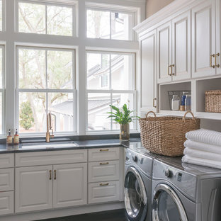 チャールストンの大きいトランジショナルスタイルのおしゃれなランドリールーム (アンダーカウンターシンク、レイズドパネル扉のキャビネット、白いキャビネット、茶色い壁、濃色無垢フローリング、左右配置の洗濯機・乾燥機、黒い床) の写真