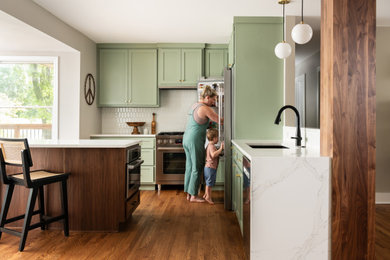 Inspiration for a medium sized retro l-shaped kitchen/diner in St Louis with a submerged sink, shaker cabinets, green cabinets, engineered stone countertops, white splashback, ceramic splashback, stainless steel appliances, light hardwood flooring, an island, brown floors and white worktops.