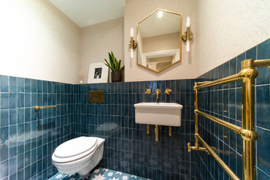 ロンドンにある高級な中くらいなトランジショナルスタイルのおしゃれなトイレ・洗面所 (壁掛け式トイレ、青いタイル、磁器タイル、磁器タイルの床、壁付け型シンク、青い床、壁紙、ピンクの壁) の写真