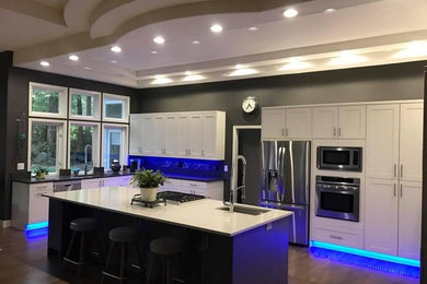 Example of a mid-sized trendy l-shaped medium tone wood floor and brown floor kitchen design in Seattle with an undermount sink, recessed-panel cabinets, white cabinets, quartz countertops, multicolored backsplash, matchstick tile backsplash, stainless steel appliances and an island