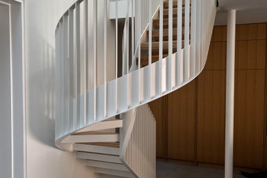 Photo of a modern wood curved metal railing staircase spindle in London with wood risers.