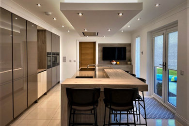 Photo of a modern single-wall kitchen/diner in Other with a double-bowl sink, flat-panel cabinets, grey cabinets, quartz worktops, black appliances, an island, white floors and brown worktops.