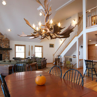 Idée de décoration pour une salle à manger ouverte sur le salon chalet de taille moyenne avec un mur blanc, un sol en bois clair, une cheminée d'angle et un manteau de cheminée en pierre.