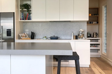 Mid-sized modern galley kitchen pantry in Melbourne with an undermount sink, white cabinets, quartz benchtops, stone slab splashback, stainless steel appliances, light hardwood floors and with island.