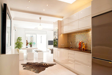 Foto de cocina lineal actual de tamaño medio abierta con armarios con paneles lisos, puertas de armario blancas, salpicadero de azulejos de vidrio, electrodomésticos de acero inoxidable y suelo de madera clara