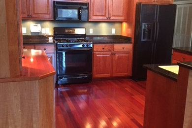 Enclosed kitchen - large traditional medium tone wood floor and brown floor enclosed kitchen idea in Other with raised-panel cabinets, medium tone wood cabinets, granite countertops, black appliances and a peninsula