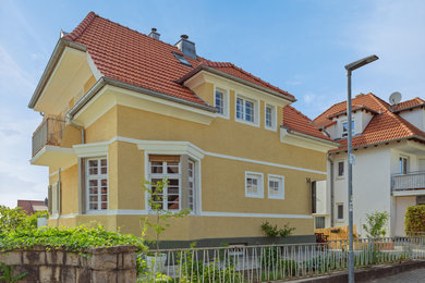 Mittelgroßes, Zweistöckiges Modernes Haus mit Putzfassade, gelber Fassadenfarbe, Halbwalmdach, Ziegeldach und rotem Dach in Sonstige